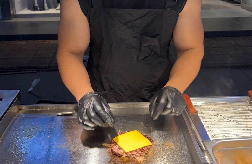 Una fetta quadrata di formaggio americano giallo posta sopra il burger caldo sulla piastra.