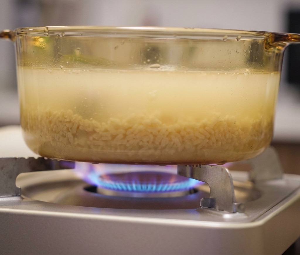 Pentola di vetro con brodo giallastro che sobbolle su una fiamma a gas blu di un fornello portatile.