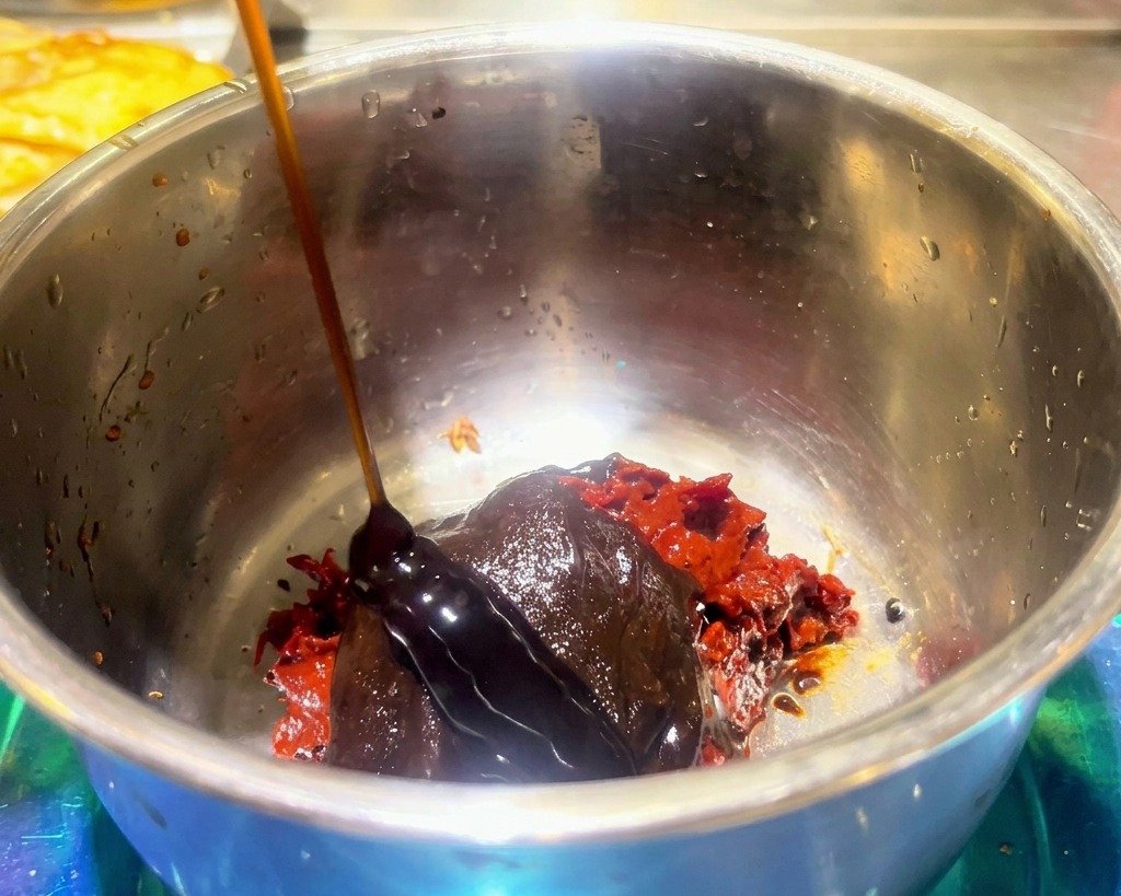 Una salsa scura e densa versata sopra la pasta di fagioli rossa e il condimento per hot pot in una ciotola.