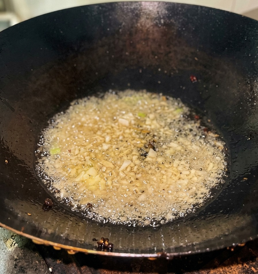 Cipollotti tritati che sfrigolano e creano bollicine nellolio caldo sul fondo di un wok di ghisa.