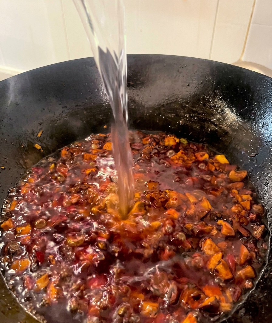 Un filo dacqua limpida versato nel wok con il condimento di pollo e funghi in cottura.