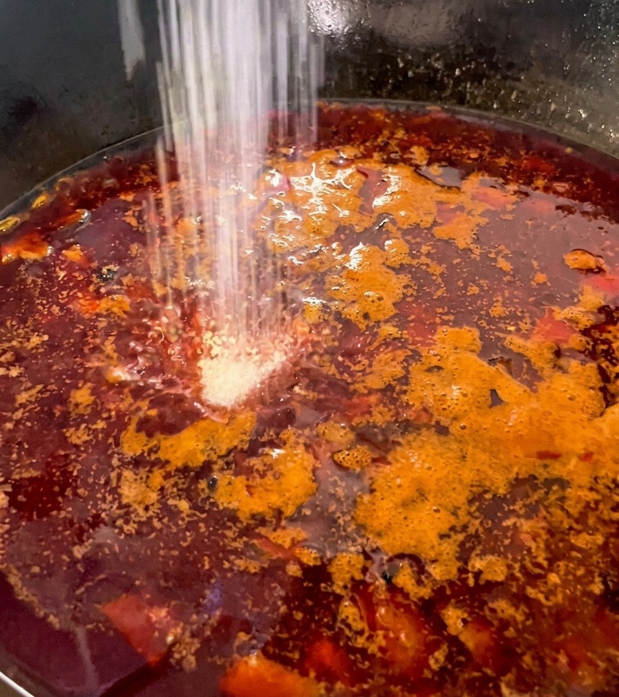 Condimento in polvere bianca spolverato sopra un sugo rosso scuro e denso con cubetti di pollo.