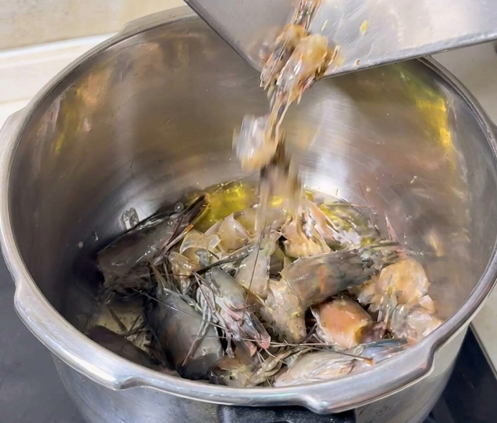 Teste e carapaci grigi di gambero versati da un vassoio di metallo in una pentola di olio bollente per essere fritti.
