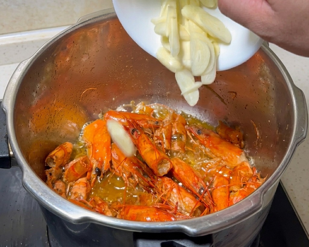 Aglio fresco a fette aggiunto da una piccola ciotola bianca nella pentola con i carapaci di gambero fritti.
