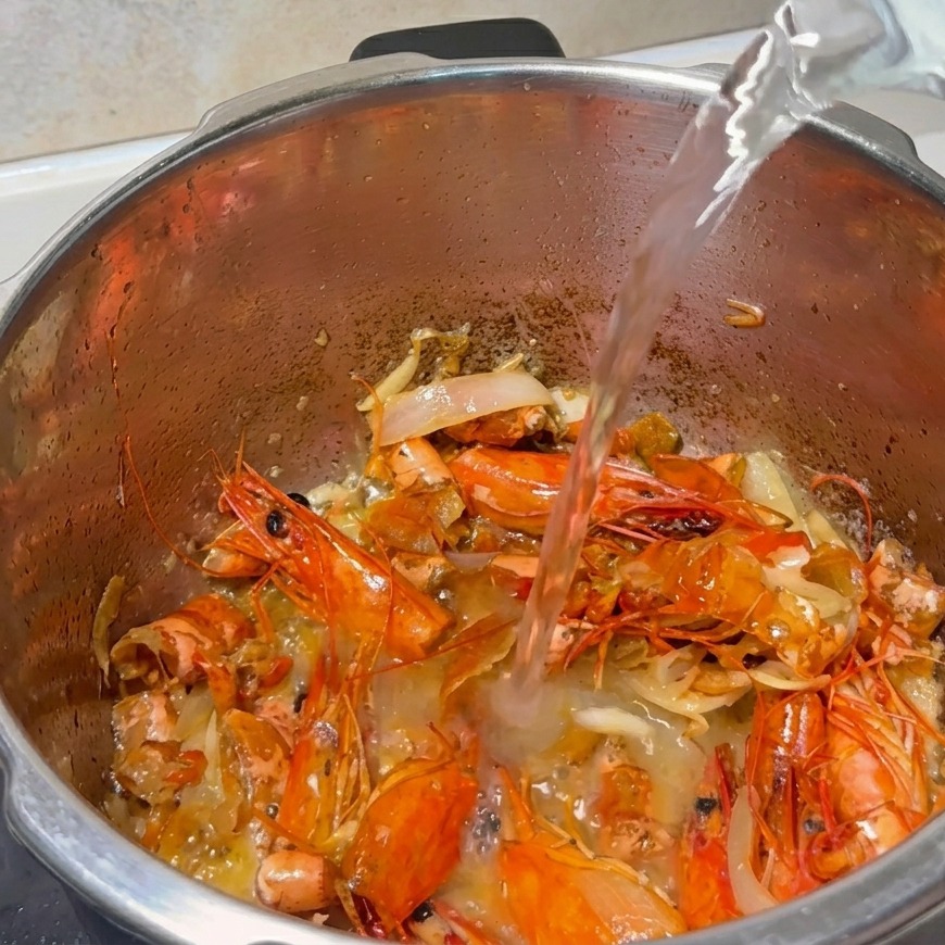 Un getto dacqua versato in una pentola piena di carapaci di gambero fritti e aromi saltati.