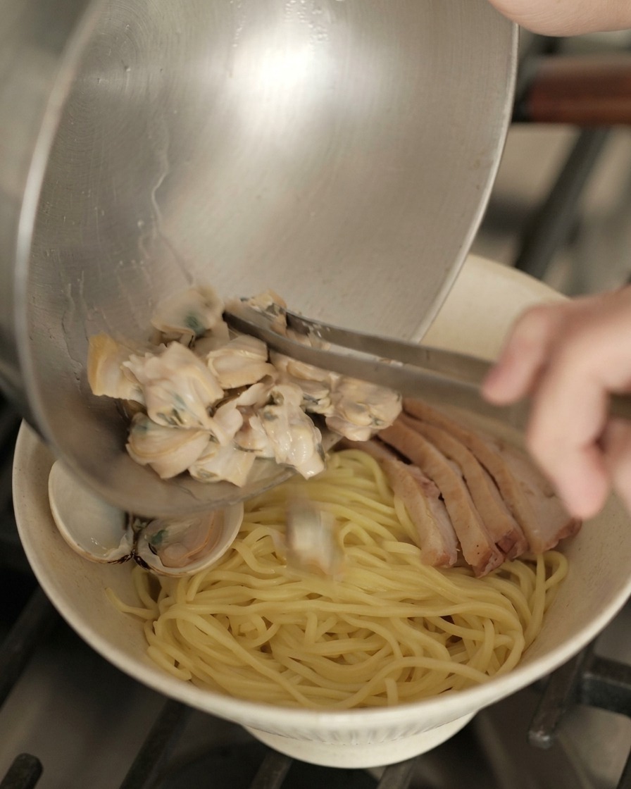 Versare le vongole cotte da una ciotola di metallo su una ciotola preparata con noodle e anatra.