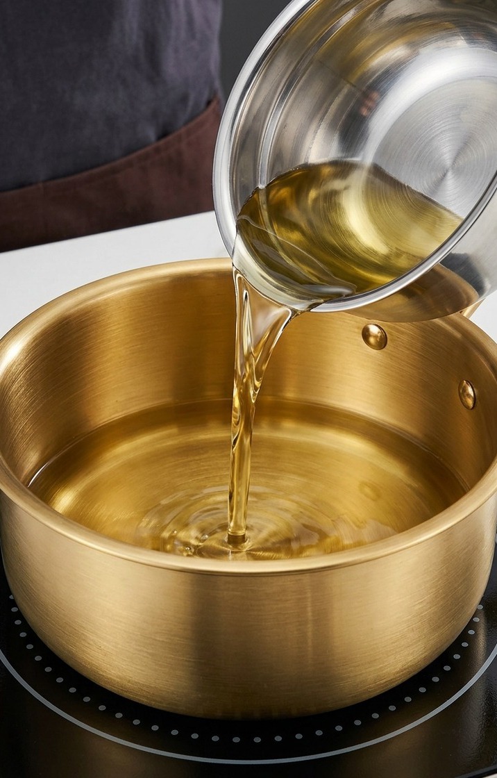 Olio di arachidi e olio di sesamo riscaldati in una grande pentola dorata su un piano a induzione.