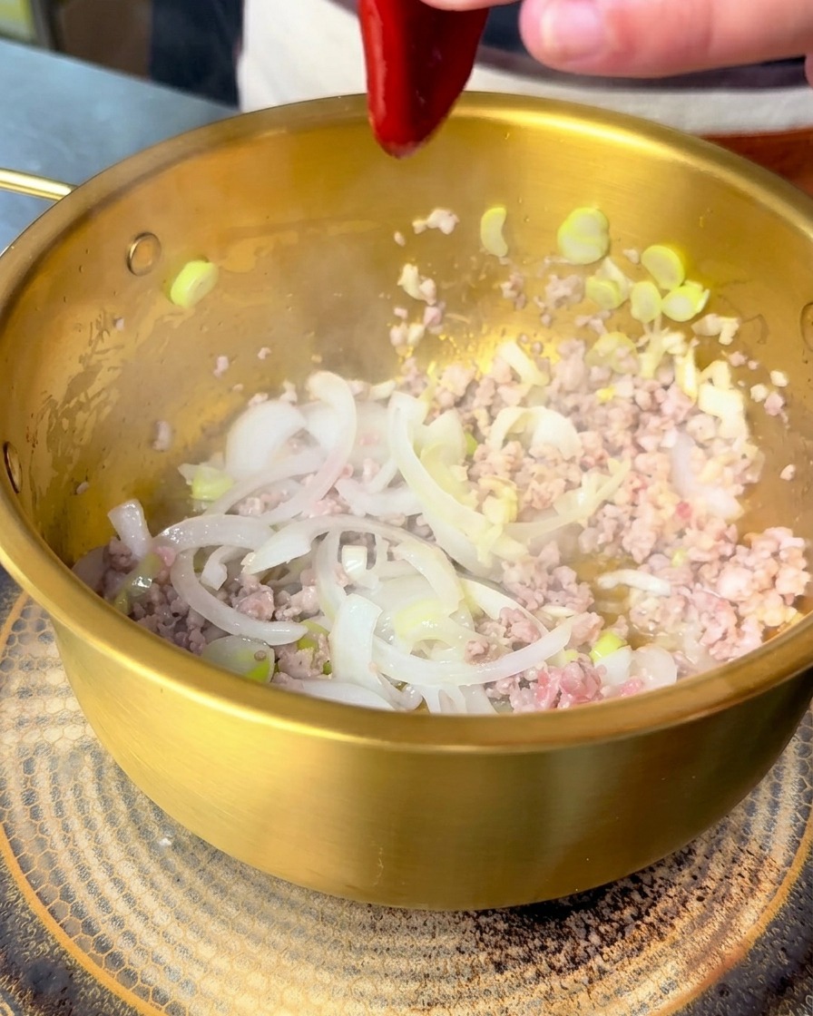 Salsa bibimbap coreana rossa spremuta in una pentola dorata con maiale e cipolle.