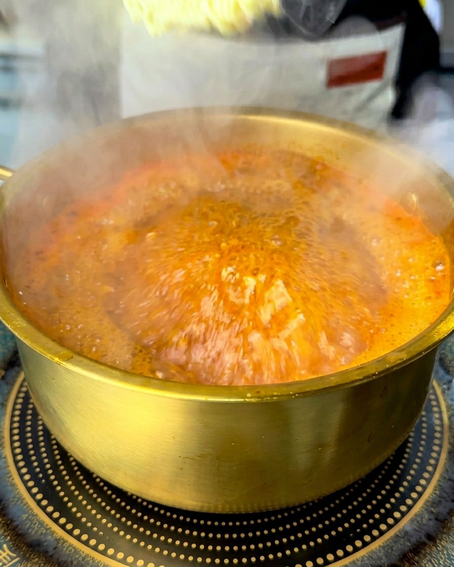Un panetto di noodle ramen istantanei secchi immerso in una pentola di zuppa rossa che bolle.