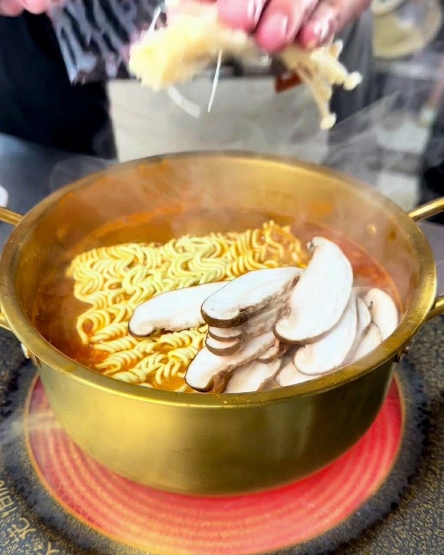 Una persona che aggiunge funghi enoki e shiitake affettati a una pentola bollente di ramen di mare.