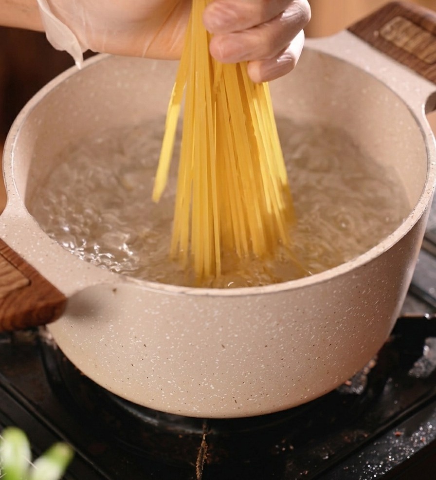 Un mazzo di spaghetti secchi immersi in una pentola di acqua bollente per la cottura.