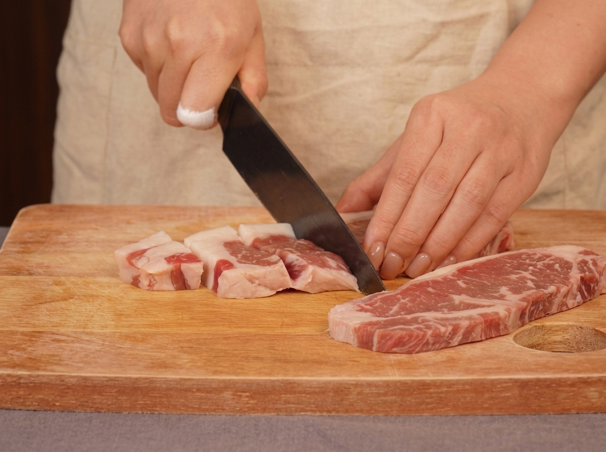 Una persona che usa un coltello da chef per tagliare della carne di manzo marezzata a cubetti su un tagliere di legno.