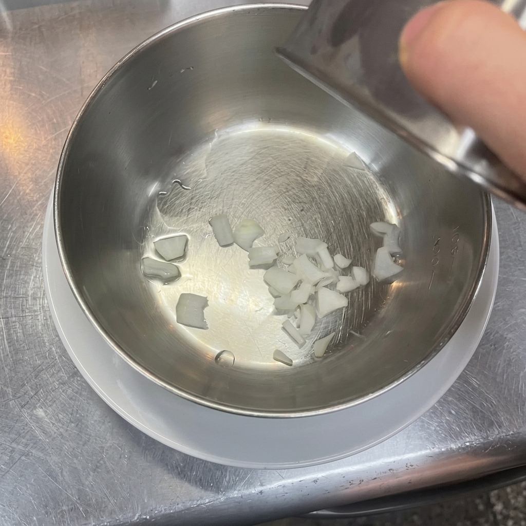 Piccoli pezzi di cipolla bianca tritata sul fondo di una ciotola pulita in acciaio inossidabile.