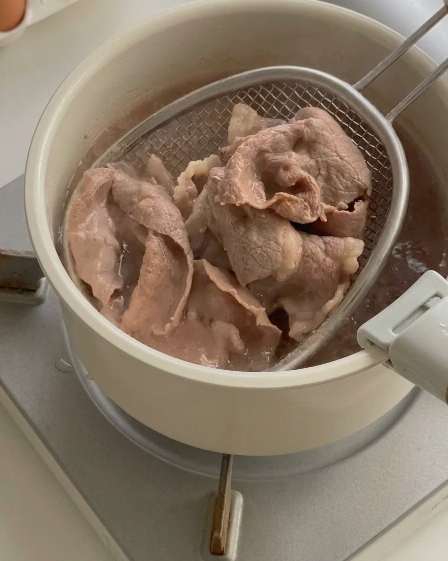 Fettine di manzo cotto sollevate da una pentola dacqua bollente con una schiumarola a rete.