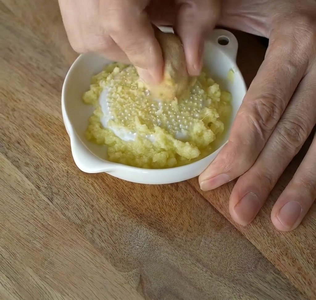 Zenzero fresco strofinato su una grattugia di ceramica bianca per creare una pasta fine.
