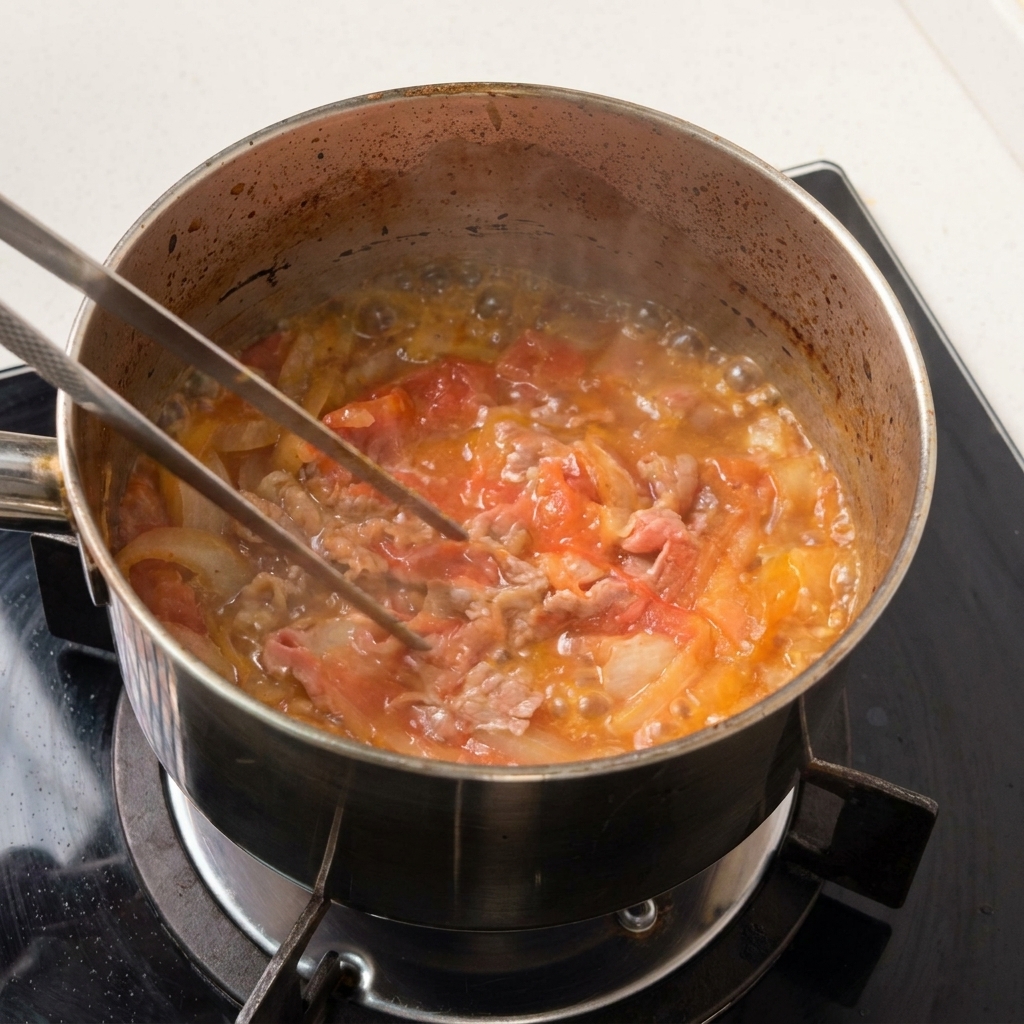 Manzo a fette sottili e cipolle sobbollono delicatamente in un fondo di liquido scuro e saporito.