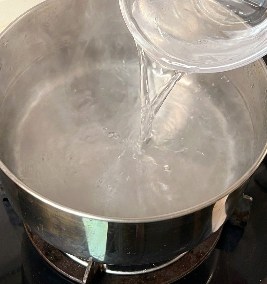 Versare una ciotolina di vetro di acqua fredda in una pentola dacciaio contenente acqua calda.