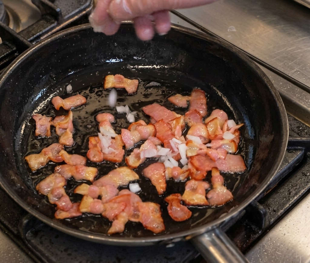 Mano che aggiunge cipolla a dadini a una padella con pancetta sfrigolante.