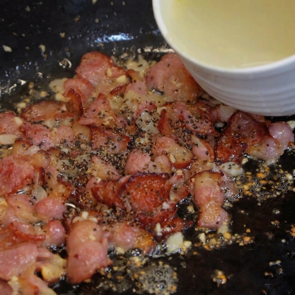 Un mestolo dacqua di cottura torbida versato in una padella con pancetta cotta.