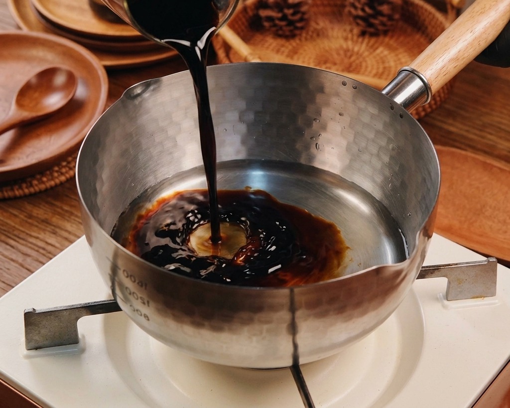 Salsa di soia versata in un pentolino dacciaio insieme ad altri liquidi.