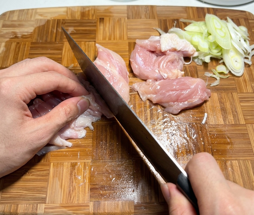 Taglio di sovracosce di pollo crude a piccoli pezzi su un tagliere di legno.