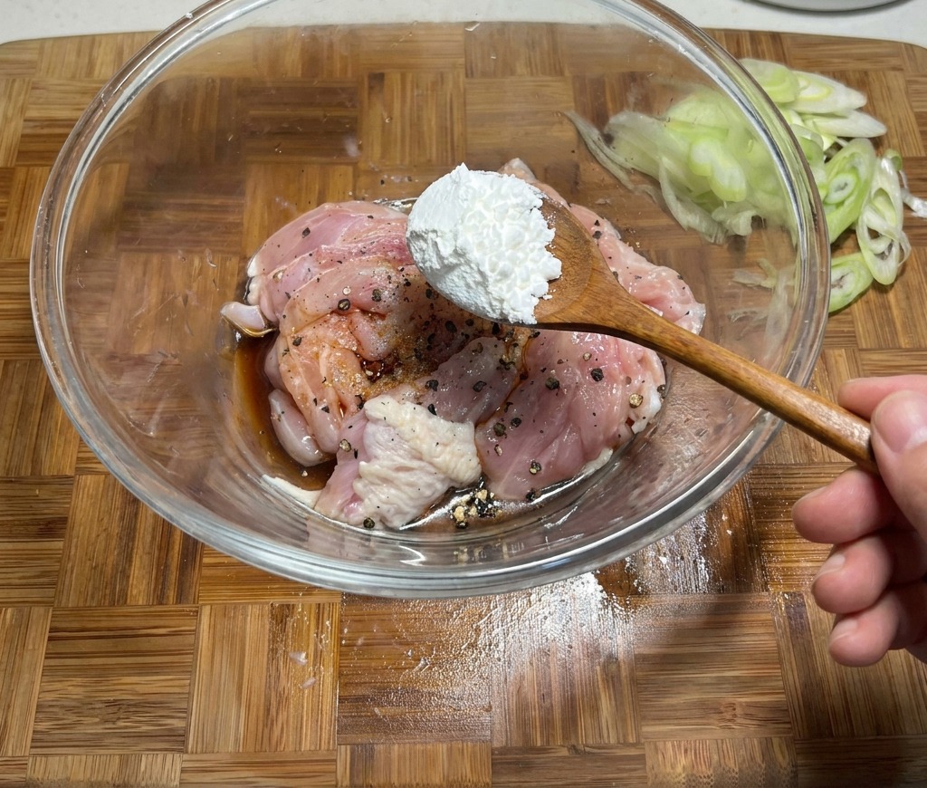 Aggiunta di un cucchiaio di amido di mais a una ciotola di pollo crudo marinato con salsa di soia e spezie.