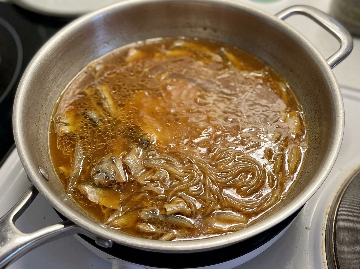 Un coperchio di vetro posizionato sopra una padella dove pollo e cipolle sobbollono in una salsa marrone saporita.