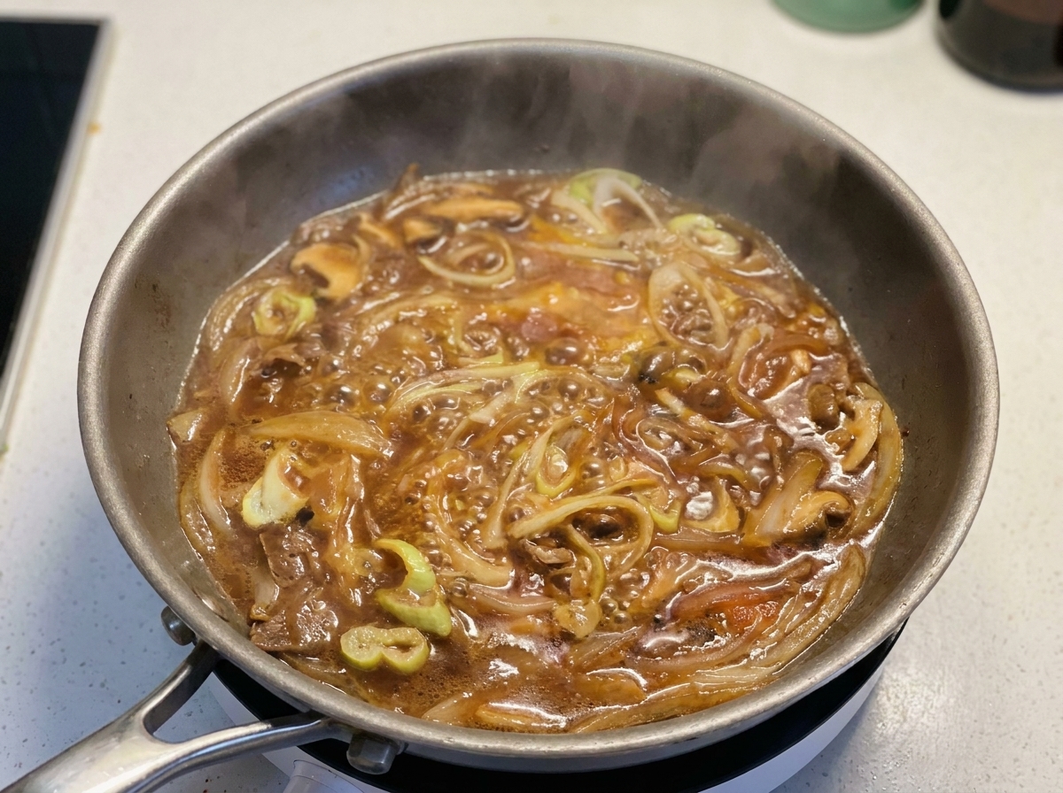 Uova sbattute versate a filo in una padella con salsa bollente, cipollotti e cipolle rosse.
