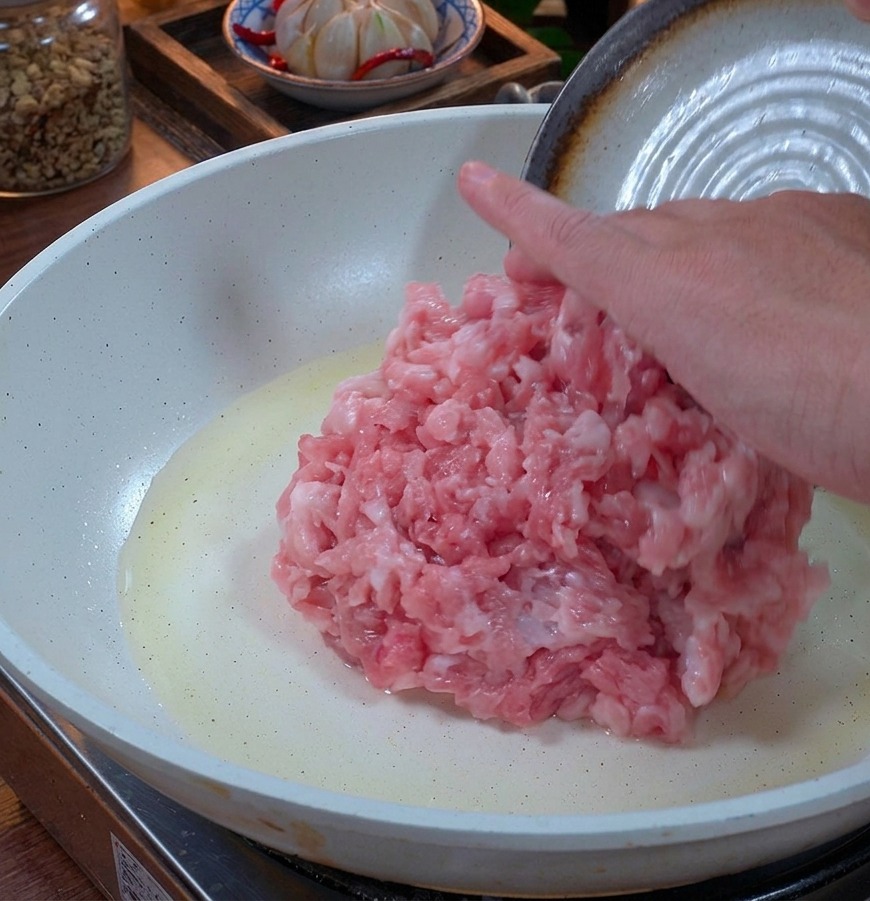 Carne macinata di maiale fresca inserita in una padella bianca con un leggero velo dolio.