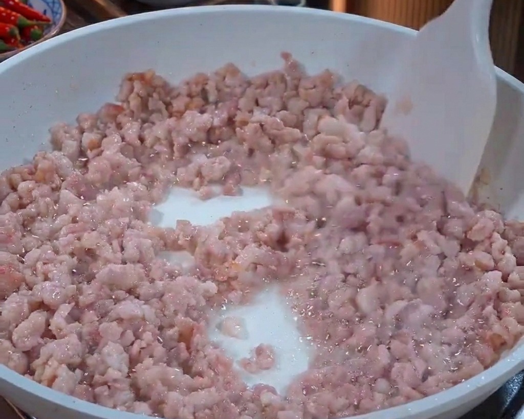 Macinato di maiale mescolato in una padella bianca con una spatola mentre cambia colore da rosa a grigio chiaro.