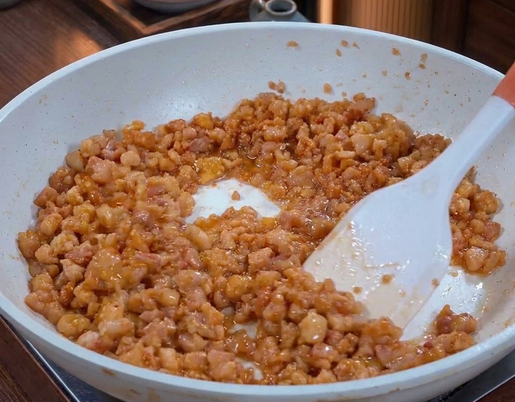 Macinato di maiale cotto in padella, lucido per il grasso sciolto e dallaspetto ben dorato e caramellato.