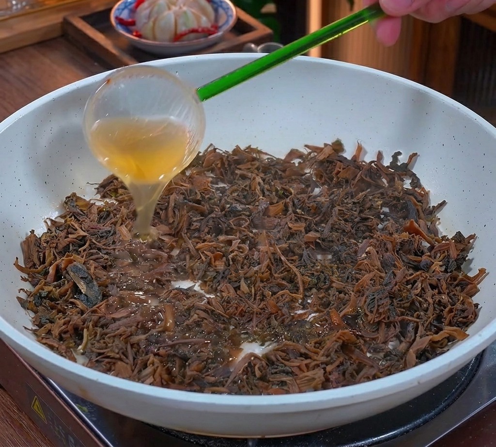 Grasso liquido dorato versato da un mestolo verde sulle verdure tritate saltate in una padella bianca.
