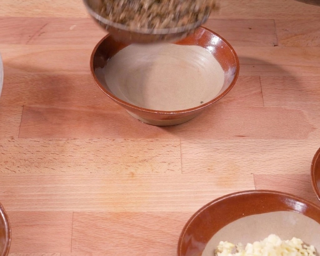 Un mestolo trasferisce il composto di maiale e verdure cotte in una ciotola di ceramica marrone su una superficie di legno.