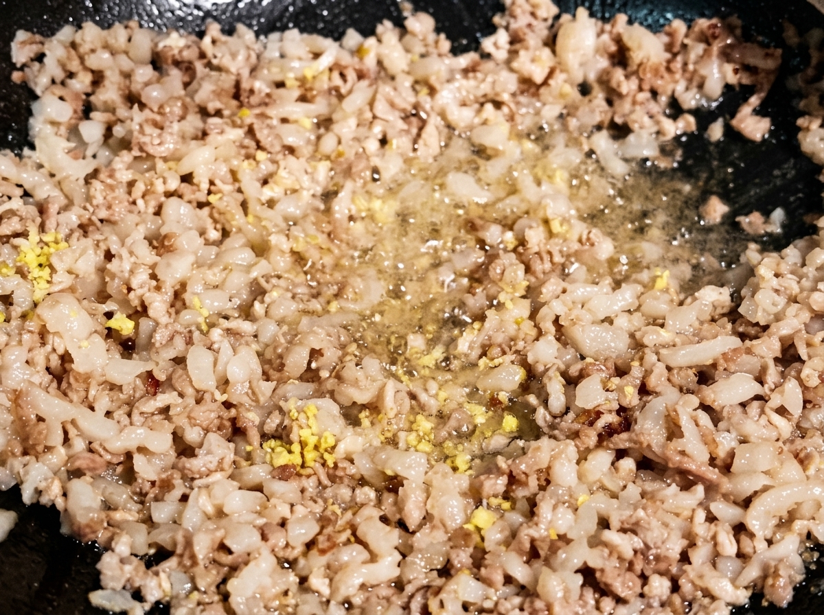 Zenzero e aglio tritati mescolati alla carne macinata rosolata in un wok scuro.