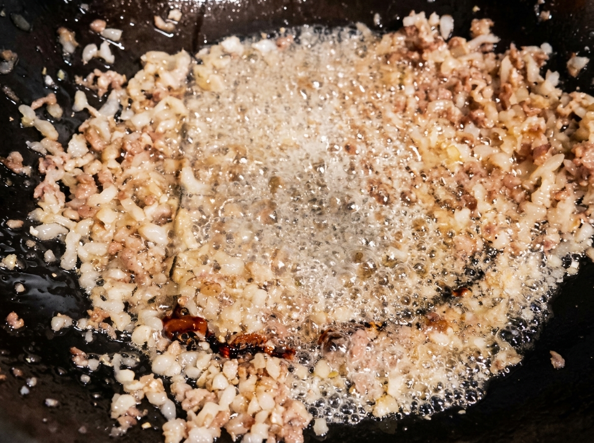 Salsa di soia chiara versata in un wok con carne macinata, il condimento sfrigola nellolio caldo.