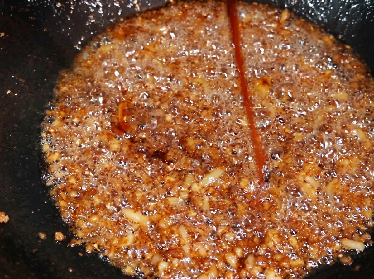 Un filo di condimento scuro al caramello viene aggiunto al maiale macinato in un wok, scurendone il colore.