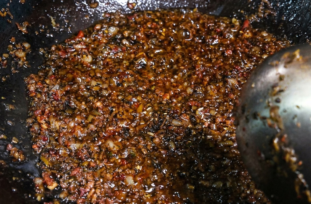 Un composto scuro e saporito di carne macinata e germogli mescolato con un mestolo in un wok dopo laggiunta dei condimenti.