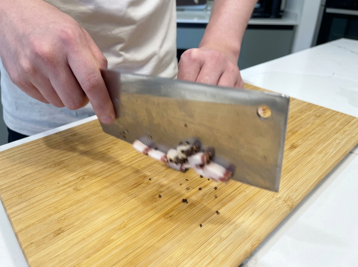 Uno chef che usa un coltello affilato per tagliare il guanciale a cubetti su un tagliere di legno.