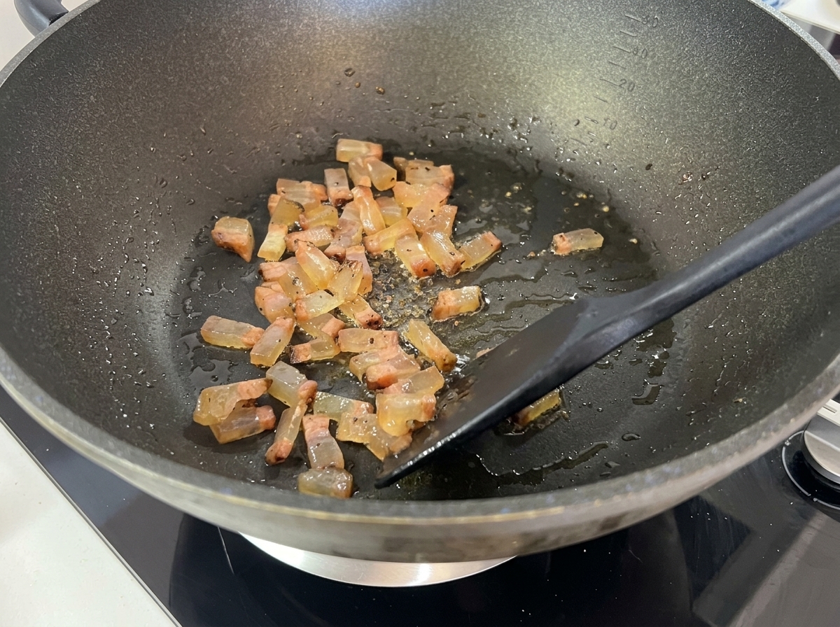 Il guanciale che soffrigge diventando croccante e trasparente in padella.