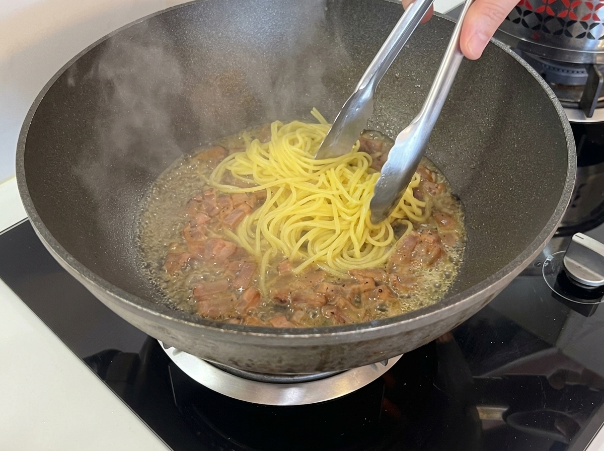 Pinze da cucina che spostano gli spaghetti dalla pentola alla padella con il guanciale.