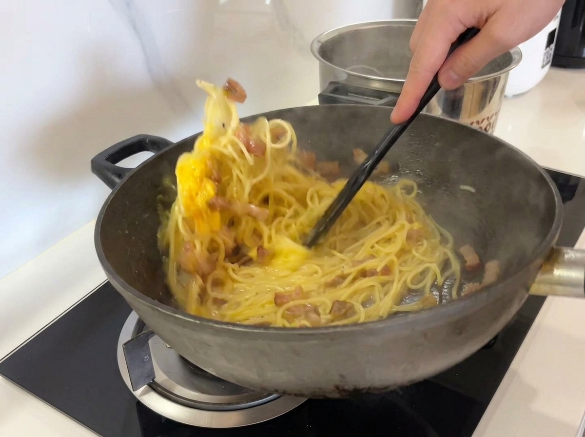 Una spatola che mescola energicamente la carbonara per distribuire luovo.