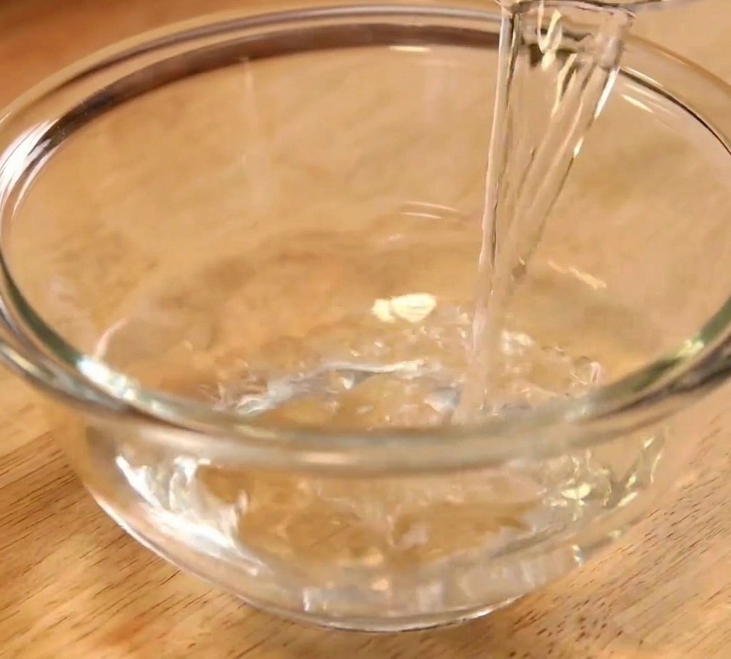 Acqua limpida viene versata in una ciotola di vetro trasparente per iniziare la preparazione della salsa.