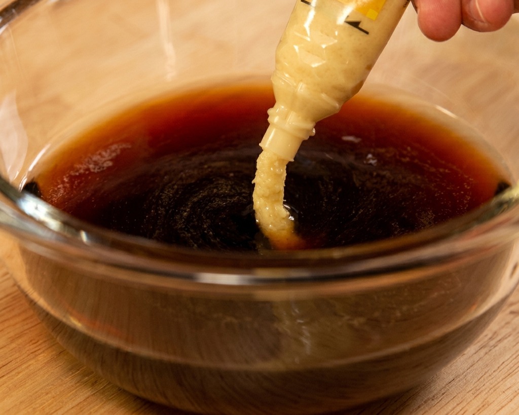 Pasta di zenzero grattugiato viene spremuta da un tubetto in una salsa scura a base di soia dentro una ciotola.