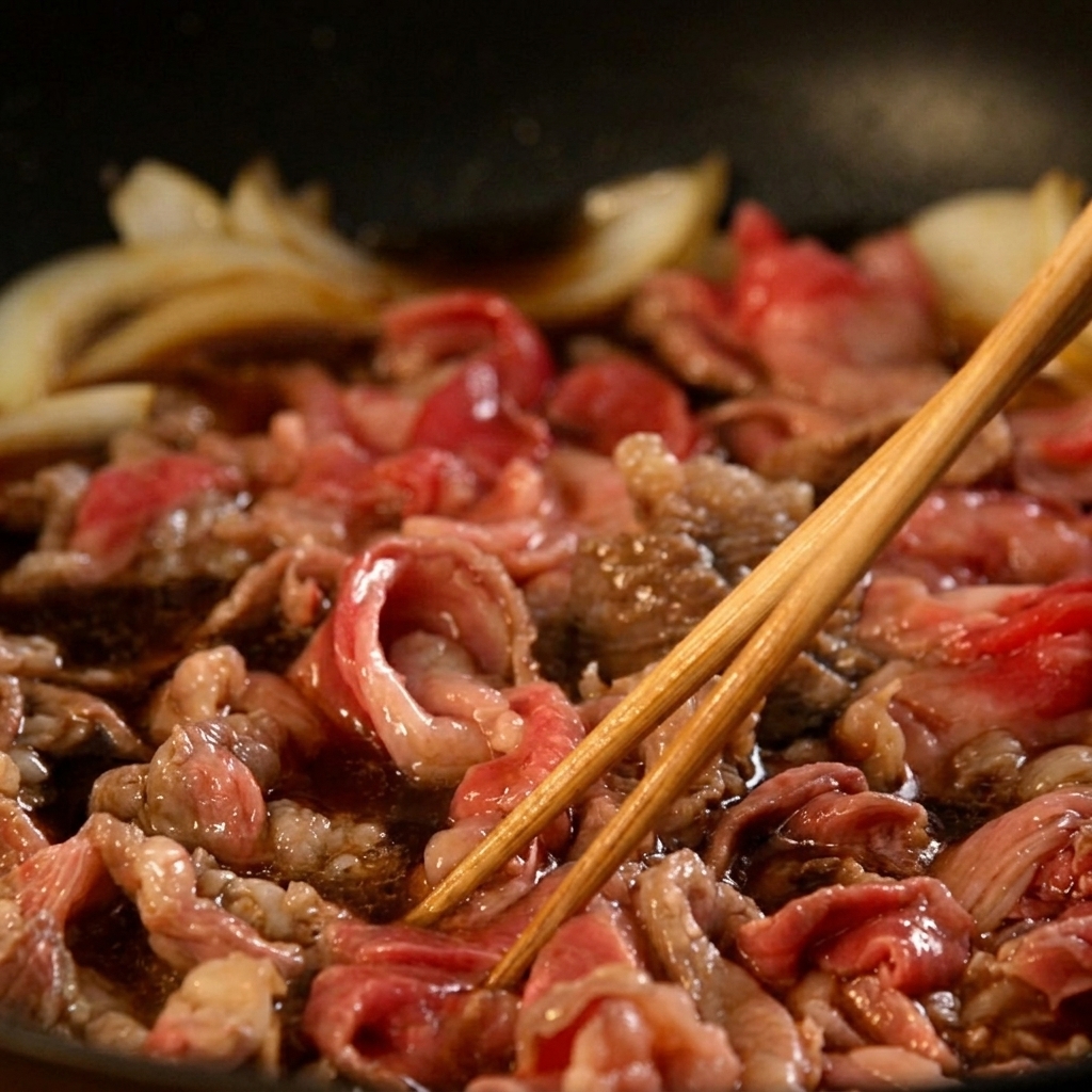 Sottili fettine di manzo e cipolle sobbollono in una salsa marrone scuro, mescolate con bacchette di legno.