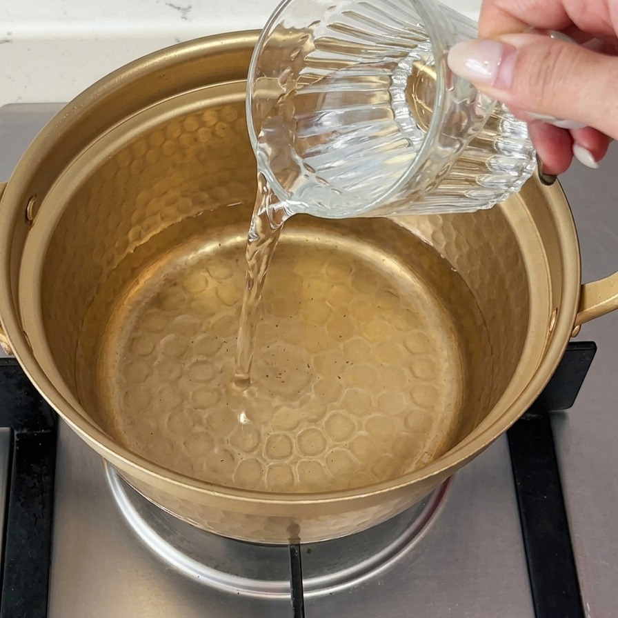 Acqua fredda versata da un bicchiere in un piccolo pentolino di metallo dorato sul fornello a gas.