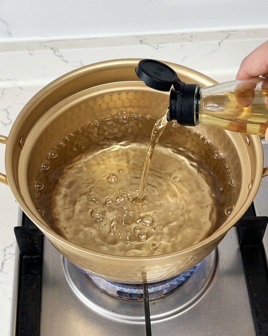 Vino limpido da cucina versato da una bottiglia di vetro in un pentolino dorato con acqua in ebollizione.