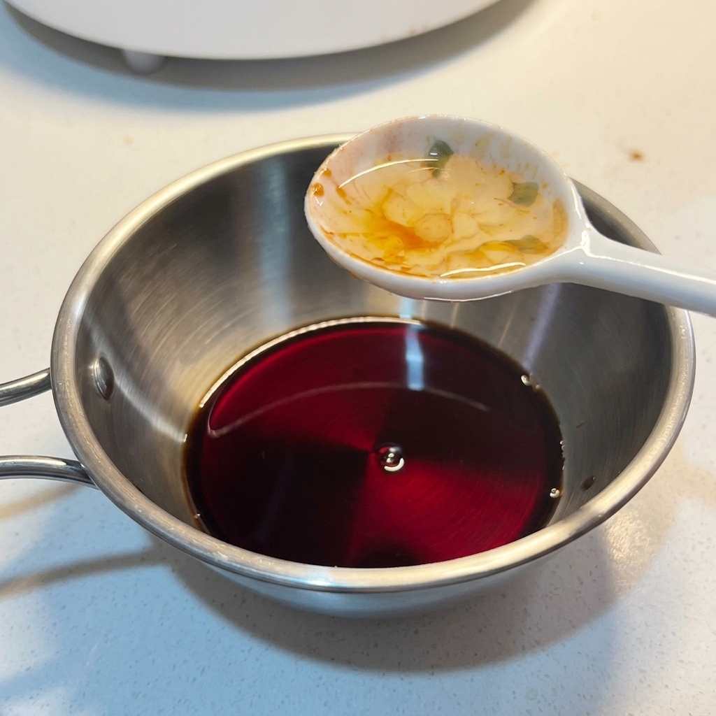 Un cucchiaio di condimento liquido che viene aggiunto in una ciotolina di metallo contenente un mix di salsa scura.