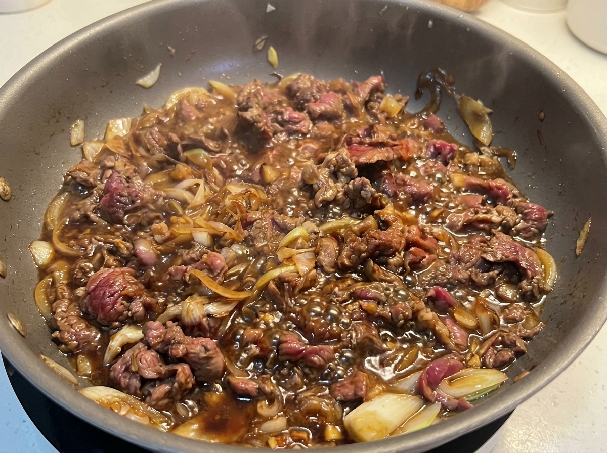 Fettine di manzo completamente cotte e dorate che sobbollono vigorosamente in una salsa scura con cipolle.
