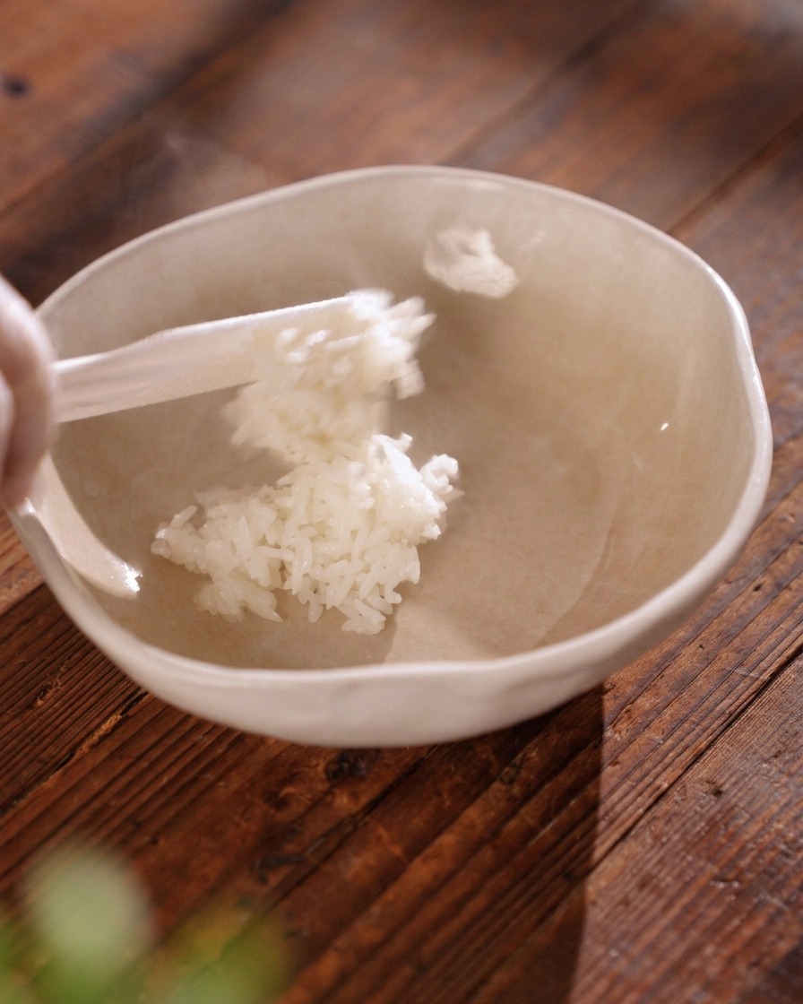 Una spatola da riso trasferisce del riso bianco fumante e ben sgranato in una ciotola di ceramica beige.
