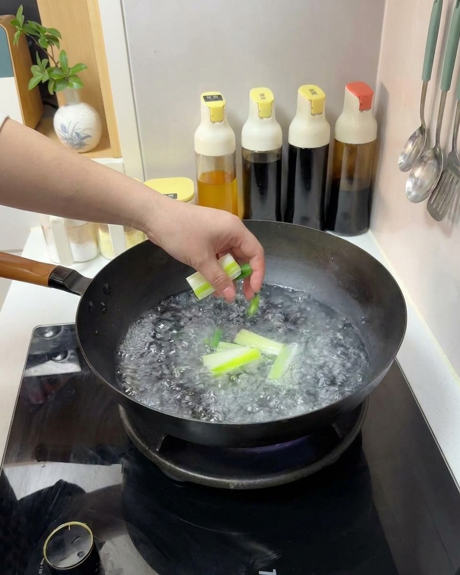 Una mano che tuffa pezzi di cipollotto tagliati in un wok di acqua bollente.